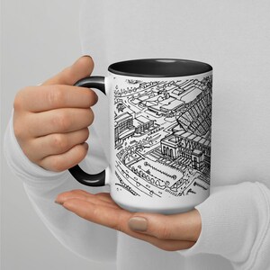 May include: A white ceramic mug with a black interior and handle. The mug features a black and white line drawing of a stadium and surrounding buildings.
