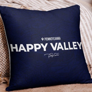Puede incluir: Una almohada azul marino con un contorno blanco de un mapa de Pensilvania. El texto "HAPPY VALLEY" está impreso en blanco en la almohada, junto con el texto "PENNSYLVANIA" y un pequeño icono de alfiler de mapa.
