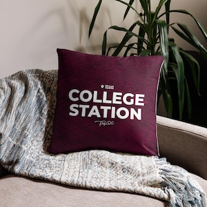 May include: A maroon throw pillow with a white graphic that says "College Station, Texas" with a signature underneath.