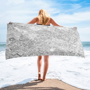 Könnte beinhalten: Ein weißes Strandtuch mit einer Schwarzweißillustration einer Stadtlandschaft. Das Handtuch wird von einer Person am Strand gehalten.