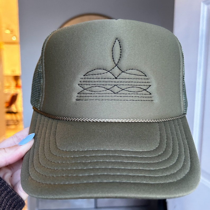 Puede incluir: Una gorra de camionero verde con un dise&ntilde;o geom&eacute;trico bordado en negro en la parte delantera. La gorra tiene una parte trasera de malla y una visera curvada.