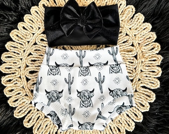 May include: Black and white patterned baby bloomers with a black bow headband. The bloomers feature a repeating pattern of highland cows, cacti, and geometric shapes.