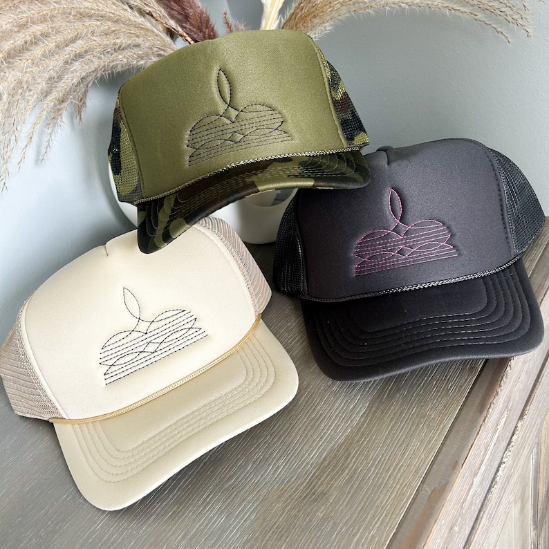 Puede incluir: Tres gorras de camionero con diferentes colores de malla en la parte posterior y dise&ntilde;os bordados. Las gorras son beige, negra y de camuflaje.