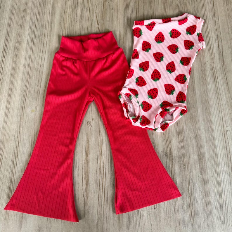 K&ouml;nnte beinhalten: Eine rote, ausgestellte Hose und ein rosa Body mit Erdbeer-Druck.