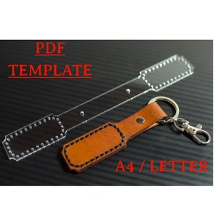 Könnte beinhalten: Eine transparente Plastikvorlage für einen Leder-Schlüsselanhänger mit einer genähten Kante. Die Vorlage ist mit "PDF TEMPLATE" und "A4/LETTER" beschriftet. Neben der Vorlage ist ein fertiger Leder-Schlüsselanhänger zu sehen.