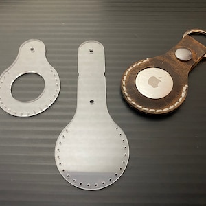 以下が含まれることがあります： 革細工用の透明なプラスチックテンプレート2枚、1枚は円形、もう1枚は涙滴型、そして銀色のリンゴのロゴが付いた茶色の革製のキーホルダーです。