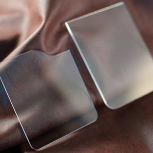 Puede incluir: Dos porta tarjetas de plástico transparente sobre un fondo de tela marrón. Los porta tarjetas son rectangulares y tienen esquinas redondeadas.