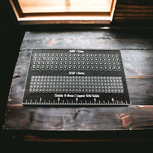 Peut inclure: Un guide de grille de disposition noir et blanc avec deux rangées de cercles. La rangée supérieure est étiquetée "9/32" 17 mm et la rangée inférieure est étiquetée "3/16" 15 mm. Le guide est étiqueté "Thistle & Bone | Layout Grid Guide" et comporte une règle avec des marques de 1 à 5.