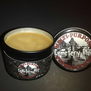 May include: A black tin container with a white label that reads "Multi-Purpose Cemetery Plot Putrescence". The container is filled with a light brown substance.