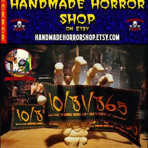 Pode incluir: Uma mão esquelética segura dois remendos de tecido preto e verde com costuras laranja. Os remendos têm o texto "10/31/365" e "HANDMADE HORROR SHOP WWW.TOXIN245.NET".