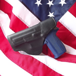 May include: A black leather holster with a blue handgun on top of an American flag.