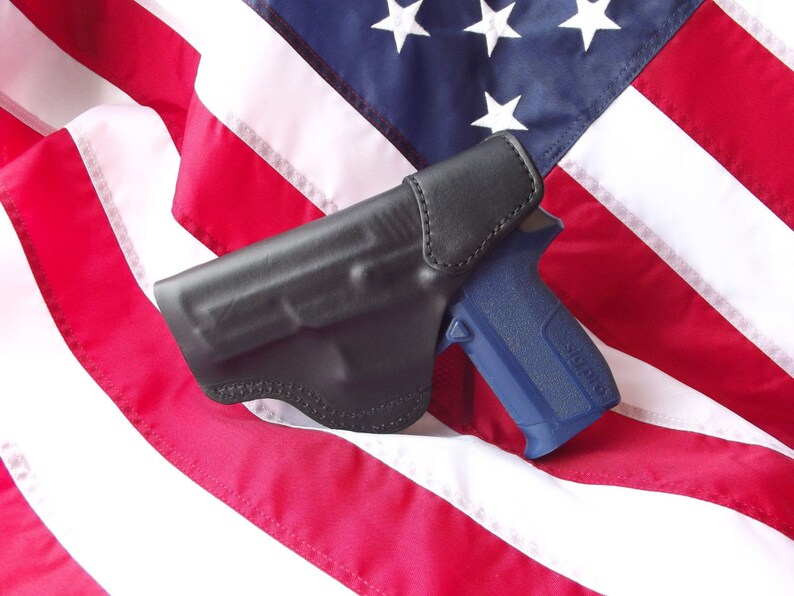 May include: A black leather holster with a blue handgun on top of an American flag.