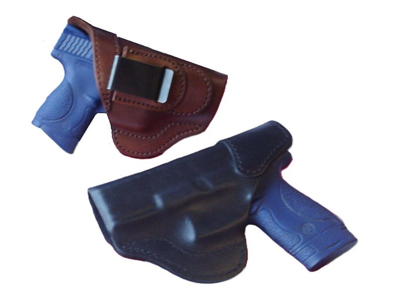 May include: Two leather gun holsters. One is brown with a black clip, and the other is black. Both holsters have a blue gun inside. The holsters are designed to securely hold a firearm.