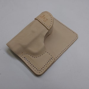 May include: A light beige leather holster with a stitched design and the initials "J & T" embossed on the top flap.