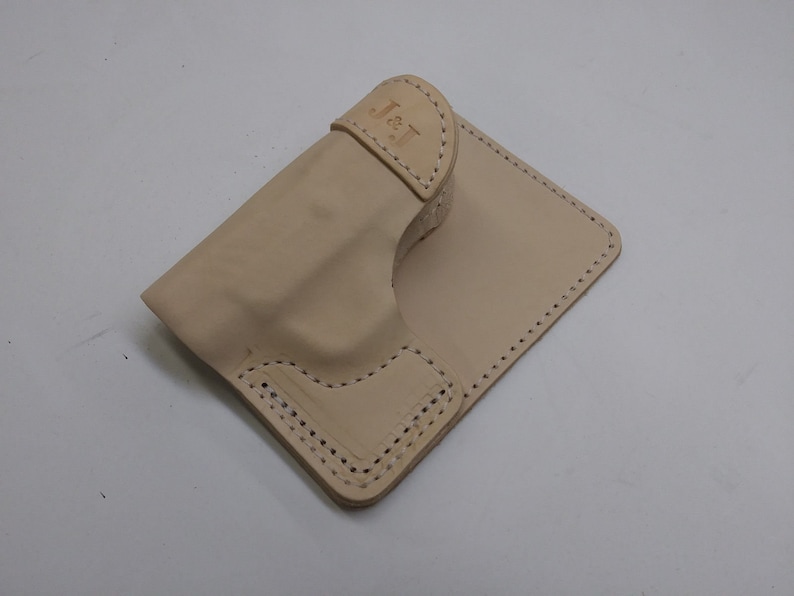 May include: A light beige leather holster with a stitched design and the initials "J & T" embossed on the top flap.