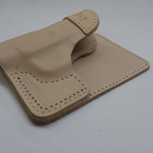 May include: A light brown leather holster with stitching around the edges. The holster is folded in half and the top flap is folded over.