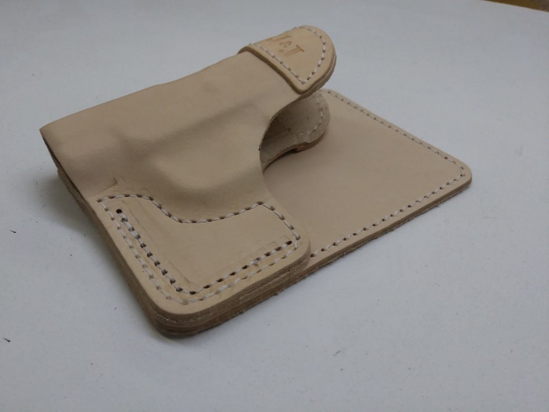 May include: A light brown leather holster with stitching around the edges. The holster is folded in half and the top flap is folded over.