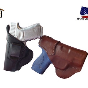 May include: Two leather holsters for handguns. The holster on the left is black and the holster on the right is brown. Both holsters are made in the USA.