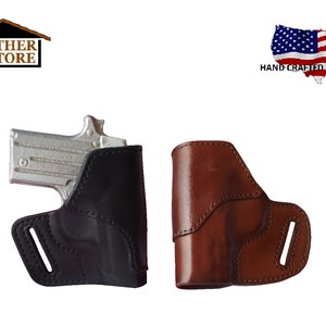 May include: Two leather gun holsters, one black and one brown, are displayed. The black holster is on the left, and the brown holster is on the right. The holsters are designed to hold a small handgun. The image includes the text "HAND CRAFTED IN THE USA".