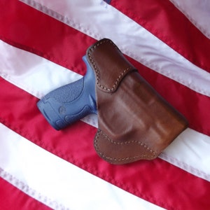 May include: A brown leather holster for a blue handgun, resting on a red, white, and blue American flag.