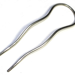 May include: A silver hair clip with a wavy design. The clip is open at the top and has two prongs at the bottom.