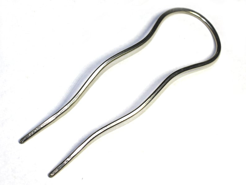 May include: A silver hair clip with a wavy design. The clip is open at the top and has two prongs at the bottom.