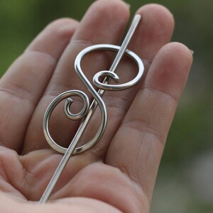 May include: A silver treble clef hair clip with a long, straight pin.