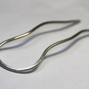 May include: A silver hair clip with a wavy design. The clip is made of metal and has a smooth finish.