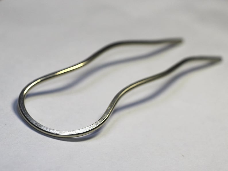 May include: A silver hair clip with a wavy design. The clip is made of metal and has a smooth finish.