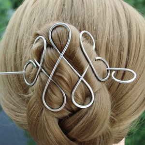 Puede incluir: Pinza para el pelo de plata con un diseño de nudo decorativo. La pinza está hecha de alambre y tiene un pasador largo y delgado que atraviesa el cabello.