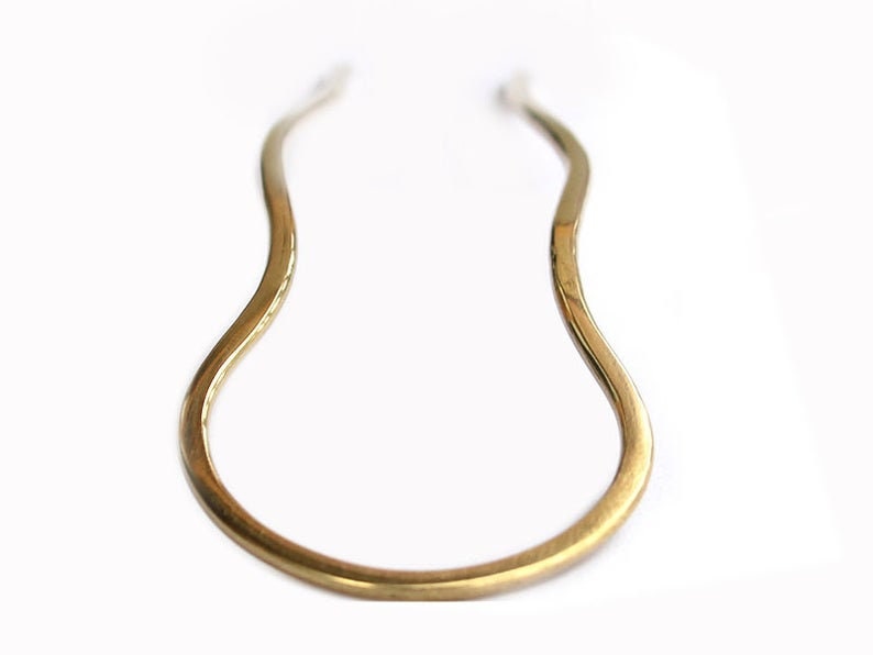 May include: A gold-colored metal hair pin with a wavy design.