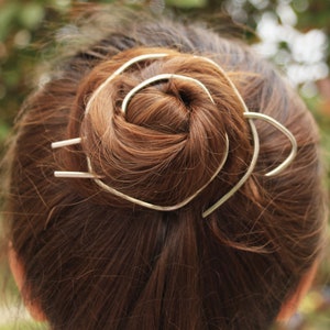 Könnte beinhalten: Ein silberner Haarknotenhalter mit Spiraldesign. Der Halter hat die Form eines Kreises mit zwei nach außen ragenden Zacken.