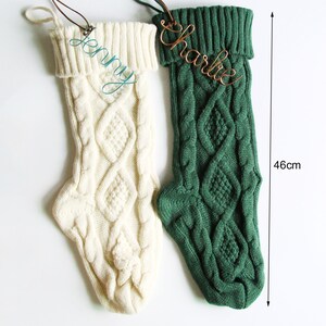 May include: Two cable-knit Christmas stockings, one cream and one green, each with a name tag. The green stocking is 46 cm (18 inches) long. The cream stocking has the name "Jenny" in cursive, and the green stocking has the name "Charlie".