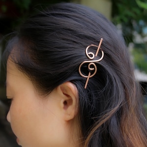 May include: A rose gold hair clip with a double swirl design. The clip is made of metal and has a simple, elegant look.