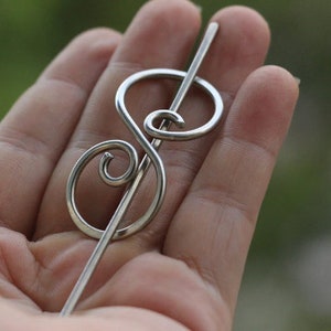 May include: Silver hair stick with a treble clef design. The stick is thin and straight with a decorative treble clef at the top.