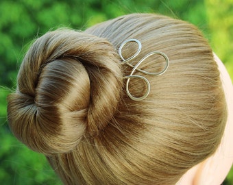 May include: A silver hair clip with a simple, elegant design. The clip is made of twisted wire and has a delicate, flowing shape.