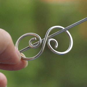 May include: A silver hair clip with a decorative swirl design. The clip is made of wire and has a simple, elegant look.