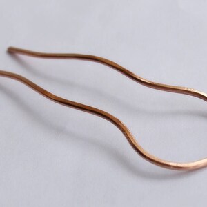 May include: A copper hair pin with a wavy design. The pin is about 10 inches long and has a smooth finish.