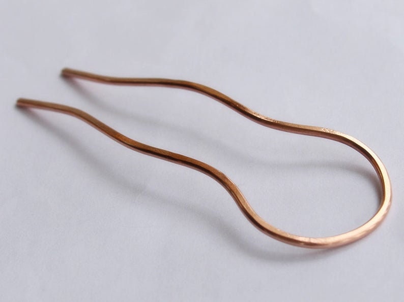 May include: A copper hair pin with a wavy design. The pin is about 10 inches long and has a smooth finish.