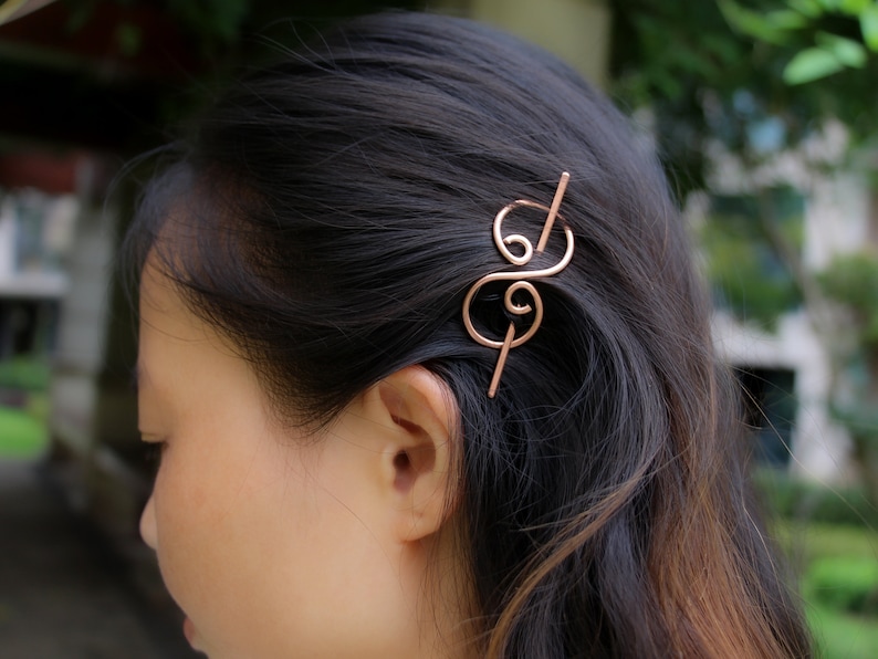 May include: A rose gold hair clip with a double swirl design. The clip is made of metal and has a simple, elegant look.