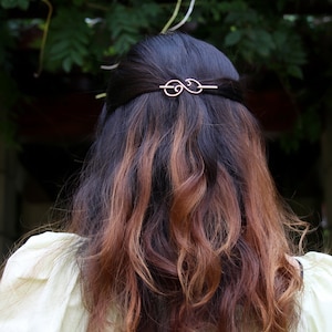 May include: A woman with long, brown hair with highlights, wearing a white blouse, with a gold hair clip in her hair.
