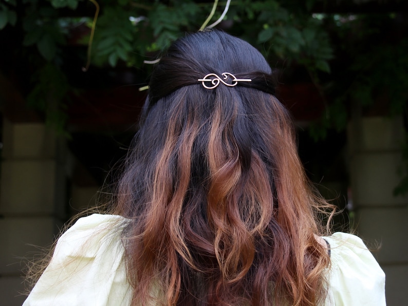 May include: A woman with long, brown hair with highlights, wearing a white blouse, with a gold hair clip in her hair.
