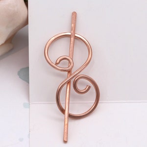 May include: Rose gold hair stick with a decorative swirl design.