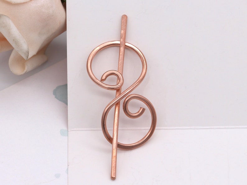 May include: Rose gold hair stick with a decorative swirl design.