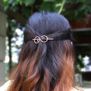 May include: A gold-toned hair clip with a swirling design. The clip is in the shape of an infinity symbol.