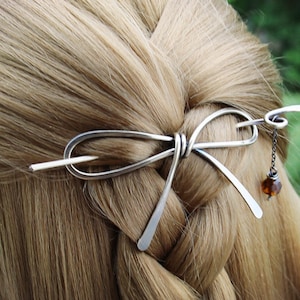 Op de afbeelding: Zilveren haarstick met een strikdesign en een hangende amberen kraal.