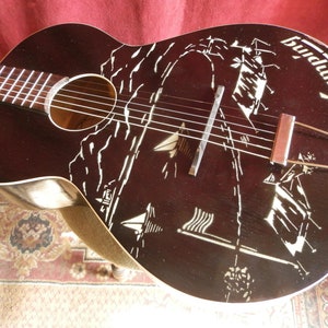 May include: A black acoustic guitar with a white design of a seascape with sailboats. The guitar has a soundhole and a bridge with strings. The word "Budd" is written on the guitar.
