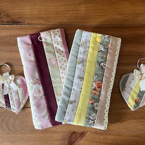 May include: Two rectangular fabric pouches and two heart-shaped keychains. One pouch features pink floral and polka dot stripes, the other has yellow bee and floral stripes. Both keychains match the pouches, featuring white bows and wooden buttons.