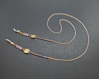 May include: Gold chain with pink and purple beads and gold circular charms attached to clear plastic eyeglass holders.