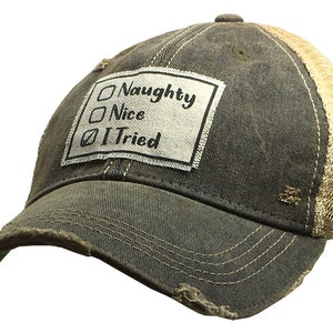 May include: A distressed black and tan trucker hat with a white patch that reads "Naughty, Nice, I Tried" with a checkmark next to "I Tried".